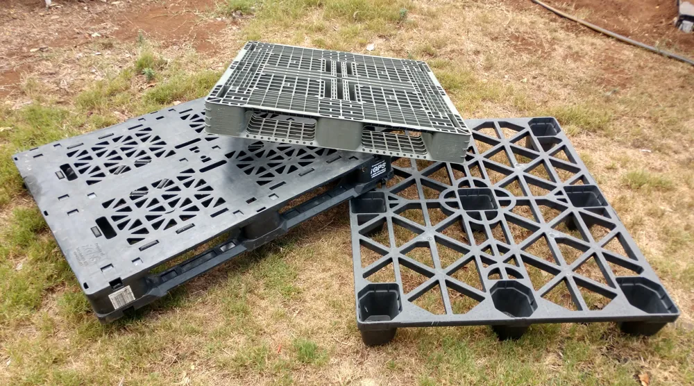 Three plastic pallets on a floor: an Asian pallet, an iGPS 48 by 40 GMA-size pallet, and an automotive skiff.