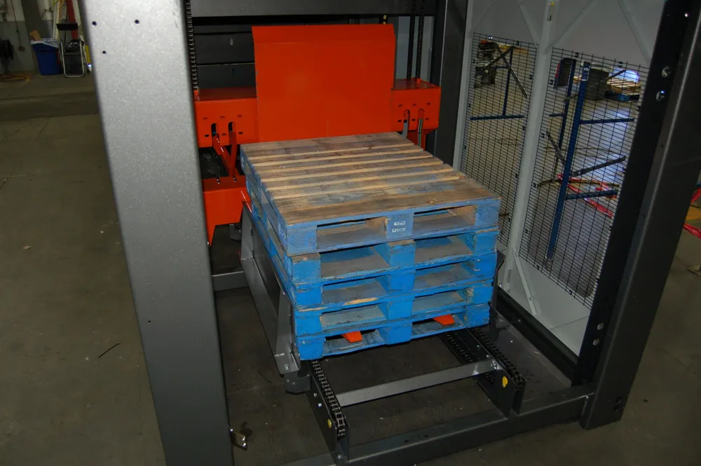 A stack of blue plastic pallets inside a fork-style pallet dispenser frame with mesh guarding.