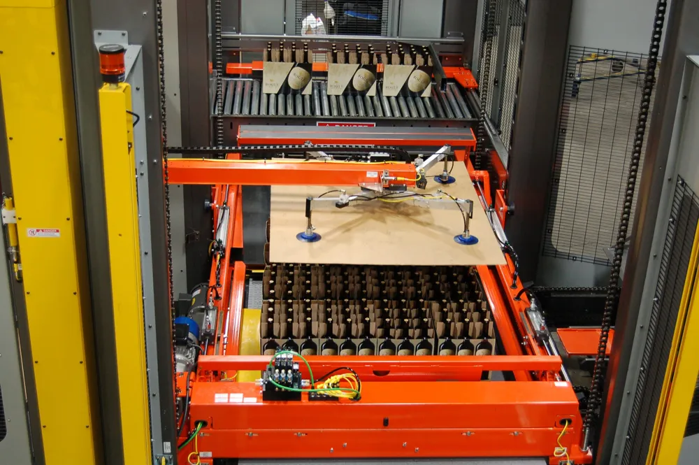 An orange sheet dispenser carriage with vacuum cups placing a brown sheet over a layer of products.