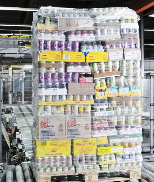 A tall stretch-wrapped pallet holding many different grocery cases, bottles, and packs.
