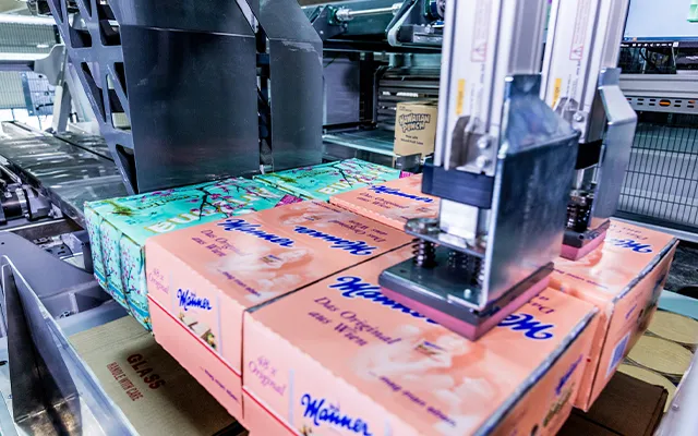 A KNAPP RUNPICK machine lowering a group of printed cases onto a stack on a conveyor.