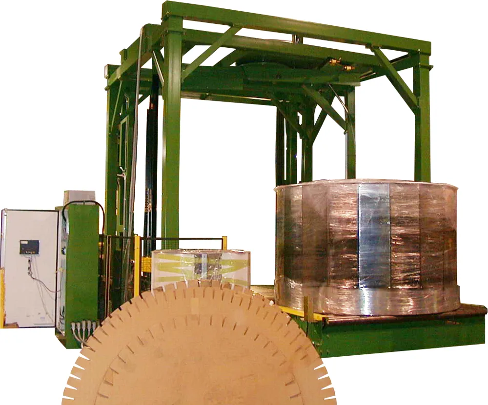 A green rotary arm stretch wrapper frame over a wrapped load, with slip sheets in the foreground.